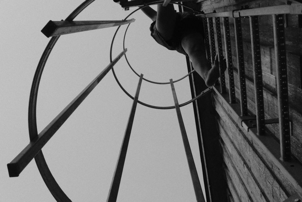 Person von unten an einer Leiter in rundem Metallgerüst (schwarz-weiß)